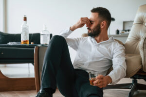 A man sitting with a drink in his hand, looking depressed and frustrated, symbolizing the struggles of addiction denial and the emotional toll it takes.