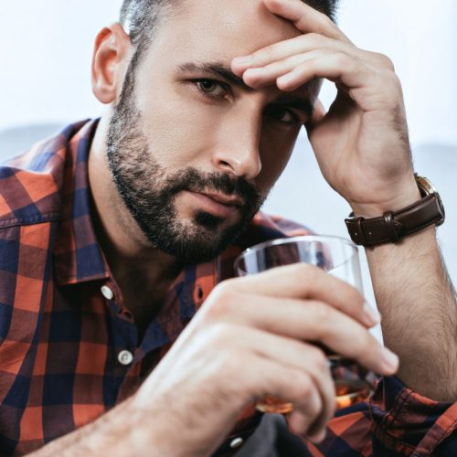 close-up portrait of depressed young man with glass of whiskey looking at camera