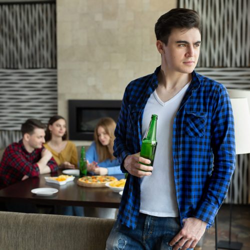 Young man drinks beer from a bottle and looks out the window in a cafe